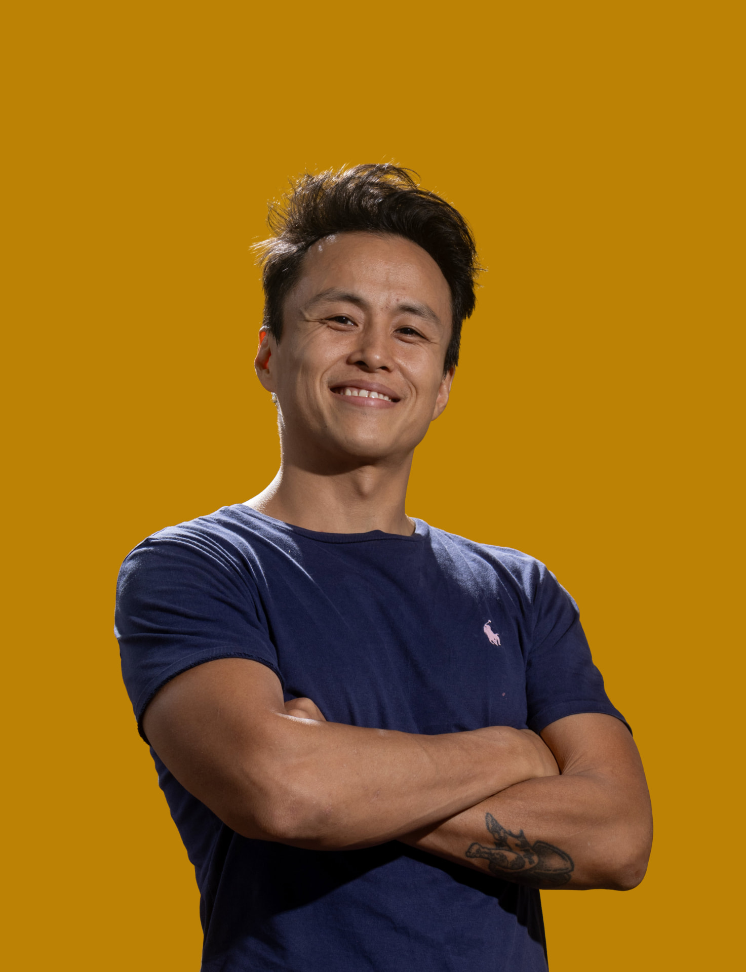 Shun Izumi de braços cruzados e sorrindo, sobre fundo amarelo